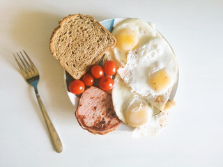 Healthy organic balanced breakfast, proper nutrition,scrambled eggs, eggs, tomatoes cherry, wholemeal bread and bacon on blue-white plate with fork lies near, top view. Instagram style