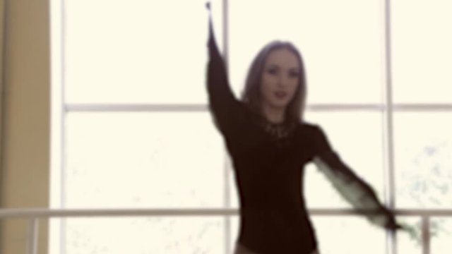Blurred frame of young beautiful brunette woman dressed in black sexy suit dancing in studio against big window.