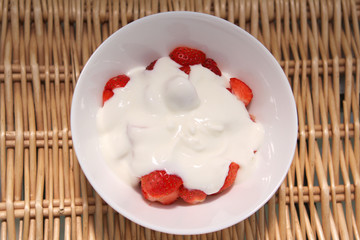 cream and strawberries in a white plate on a wicker tray, top view