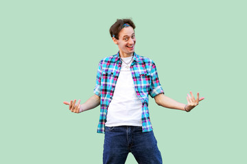 Come to me. Portrait of funny young man in casual blue checkered shirt and headband standing looking at camera and inviting to come to him with toothy smile. studio shot, isolated on green background.