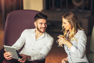 Couple Sitting In Hotel Lobby Looking At Digital Tablet