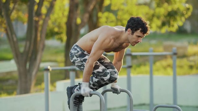 Close up sportsman doing exercises on parallel bars at athletic field
