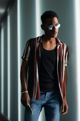 young handsome attractive guy in sunglasses poses in the neon light of the night city and using his mobile phone