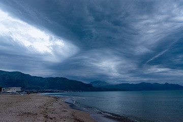 Scenic gray-blue clouds during sunrise over coastline with sandy beach and clear sea water in Alcamo Marina, small town in Sicily, Italy, summer vacation destination