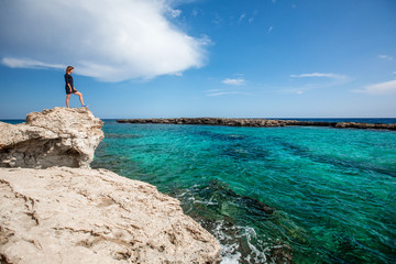 The young sporty woman the traveler in a dress costs on the bank of the beautiful blue sea.