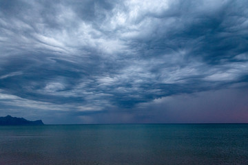 Scenic gray-blue clouds during sunrise over coastline with sandy beach and clear sea water in Alcamo Marina, small town in Sicily, Italy, summer vacation destination
