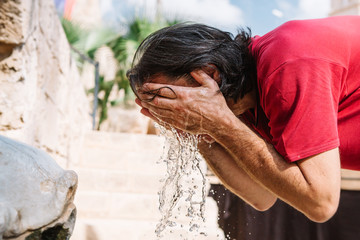 The man with dark hair overheated in the sun and freshens up with water from the fountain or a source in the ancient city.