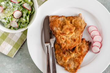 Fried pork chop in breadcrumbs served with radishes and lettuce.