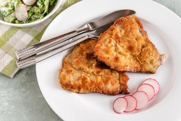Fried pork chop in breadcrumbs served with radishes and lettuce.