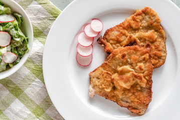 Fried pork chop in breadcrumbs served with radishes.