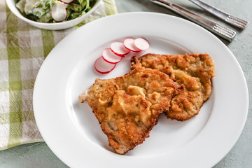 Fried pork chop in breadcrumbs served with radishes and lettuce.