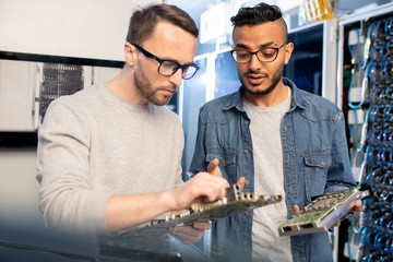 Concentrated smart young database engineers in glasses viewing circuit boards of servers while...