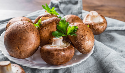 Group of whole raw fresh brown mushroom portobello on white plate. 