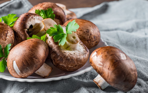 Group of whole raw fresh brown mushroom portobello on white plate. 