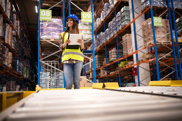 Beautiful woman worker with hardhat and checklist controlling distribution in warehouse center.