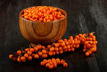 branch of sea buckthorn in wooden cup and branch on wooden background