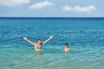 European man is happy to spend his summer holidays with his son. They are swimming in the ocean and enjoying pastime..