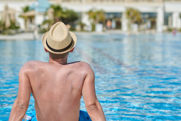 Man sitting on side of swimming pool. Back view.