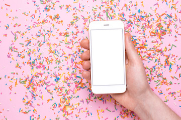 Male hands hold mobile phone mock up on a pink background with sweet multicolored sprinkles
