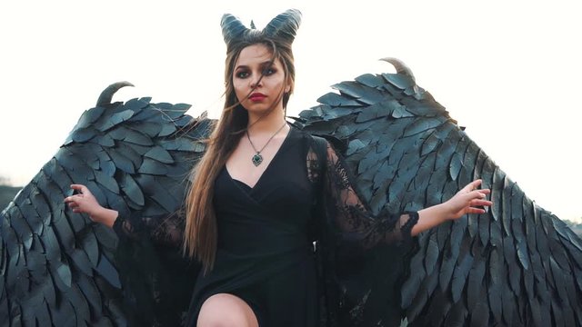 graceful lady in a long black dress with lace sleeves drops hem of dress, a dark angel with heavy strong feather wings fallen from heaven. charming fantasy image of femme fatale brings death and war