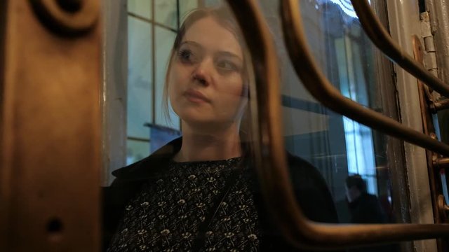 Attractive middle aged brunette woman in a black coat behind a glass vintage door. Warm, muffled light, twilight.