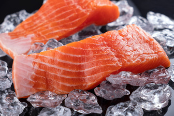 Raw salmon filet in ice on dark  background. Closeup