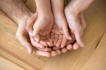 Close up of loving mom dad and kid hold hands on floor palms up