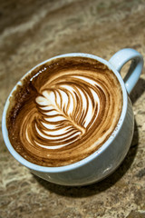 Close up white coffee cup with leaf shaped latte art foam on marble table in Brazil