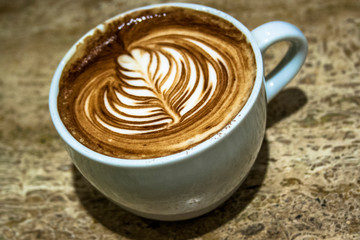 Close up white coffee cup with leaf shaped latte art foam on marble table in Brazil
