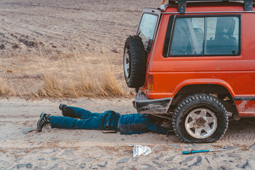 man lies under a 4x4 car on a dirt road