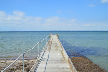Fototapeta na wymiar Empty dock, calm sea and sky background. View of wooden bridge above smooth ocean.