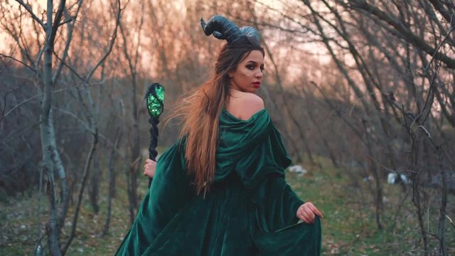 queen of the other world leads into abyss, girl with large black horns on her head is dressed in a long, amazing green velor robe with open shoulder. mysterious image of vampire with magic staff