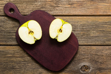 half cut green apple on chopping board, old wooden table