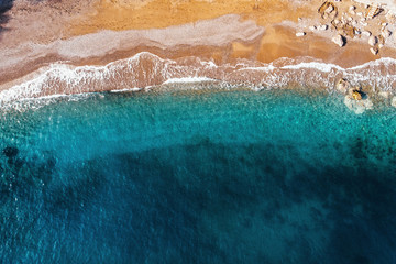 Aerial top view of azure sea waves and sandy beach coast in sunny summer day, drone photo