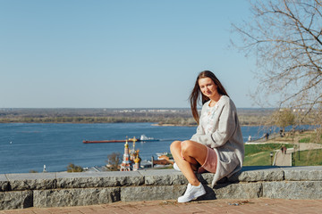 Graceful girl expression waiting friend on parapet enjoying amazing city view. Outdoor portrait of lovely brown-haired young woman.