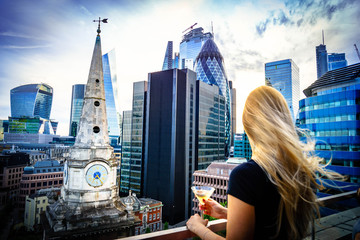 Fototapeta na wymiar Aerial view of skyscrapers of the world famous bank district of central London at sunset and woman drinking cocktail and enjoying the vi