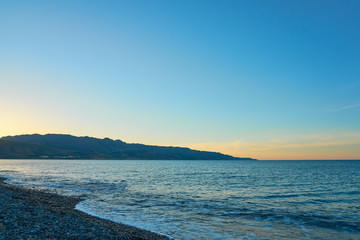 Obraz na płótnie Canvas The sunset on the pebble beach with hills on the background, Kolymbari, Crete, Greece.