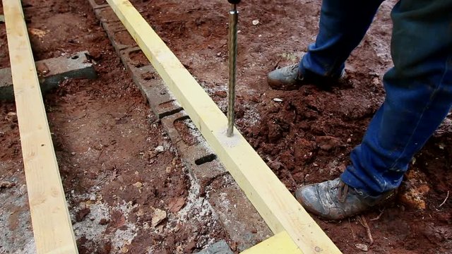 Industry worker drilling a wood rafter with a big drill. Manual making of a foundation with concrete, cinderblock and wood.