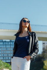 Close-up Portrait of a young beautiful fashionable woman with sunglasses. Lady posing against the city. The model wears a stylish leather jacket. women's fashion.