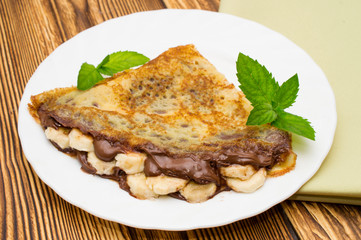 Crepes with bananas and cream on a wooden background
