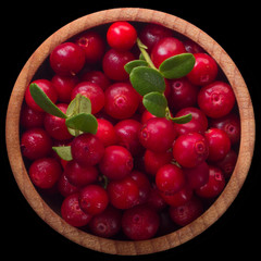 heap of cowberry in wooden cup isolated on black background. top view