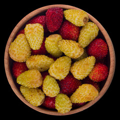 heap of red and yellow wild strawberry in wooden cup isolated on black. top view