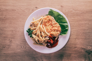 chicken fillet in cheese and French fries on white plate