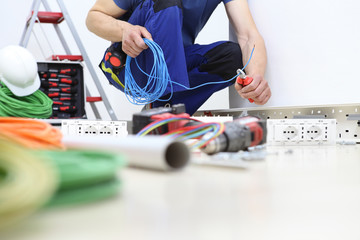 electrician at work with nippers in hand cut the electric cable, install electric circuits, electrical wiring - obrazy, fototapety, plakaty