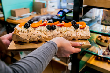 salesman in a confectionery holding a meringue cake at the counter