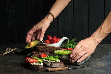 Healthy breakfast sandwich with avocado, cheese, strawberries, herbs and seeds on a dark background. An idea for bruschetta or for a healthy snack. Healthy vegan breakfast.