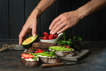 Healthy breakfast sandwich with avocado, cheese, strawberries, herbs and seeds on a dark background. An idea for bruschetta or for a healthy snack. Healthy vegan breakfast.