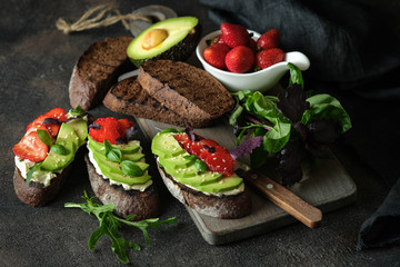 Healthy breakfast sandwich with avocado, cheese, strawberries, herbs and seeds on a dark background. An idea for bruschetta or for a healthy snack. Healthy vegan breakfast.