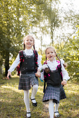 Two schoolgirls with backpacks on their shoulders run along the path in the park.