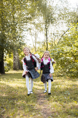 Two schoolgirls with backpacks on their shoulders run along the path in the park.